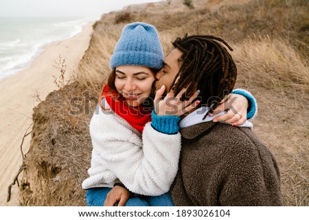 Lovely young multiethnic couple cuddling at the beach, wearing warm clothes