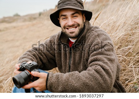 Happy handsome photographer with camera smiling while sitting outdoors