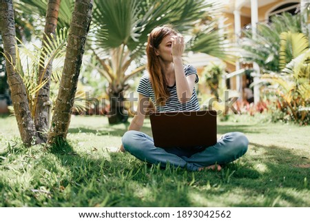 woman with laptop sitting on the grass in the park outdoors freelancer working outside the office