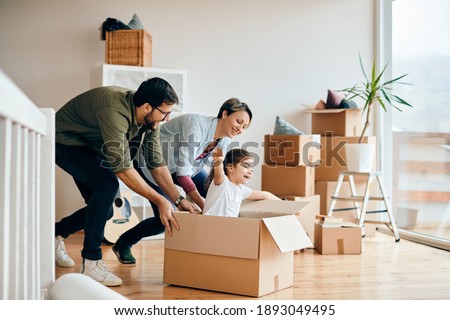 Happy parents having fun with their daughter while pushing her in carton box at their new home. Royalty-Free Stock Photo #1893049495