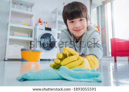 Happy Asian boy with rubber gloves is cleaning up the floor, helping family with housework. Royalty-Free Stock Photo #1893055591