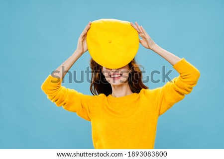smiling woman yellow sweater hat holding blue background