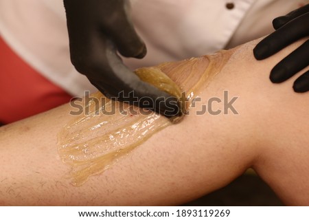 cosmetician hands make depilation procedure on woman legs with wax close up photo