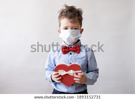 Cute little boy in bow tie with heart gift box and face mask valentine day. 