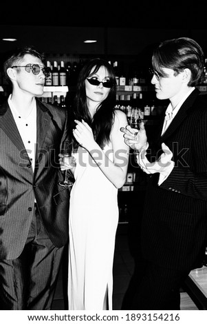 Beautiful young people, a girl and two male twins celebrating. Champagne in hands, happy emotions, New Year's mood. Retro style, black and white photo, camera flash
