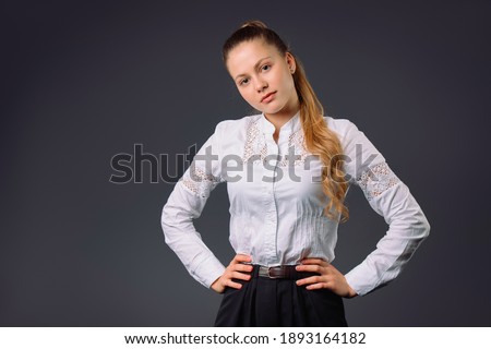 A cute business woman in a white shirt looks tenderly into the camera on a gray background with side space. Young entrepreneurs concept.