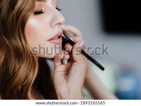 A beautiful young woman with long hair doing makeup for a wedding or photo shoot. the work of a make-up artist. the morning of the bride. decorative cosmetics. Royalty-Free Stock Photo #1893165565
