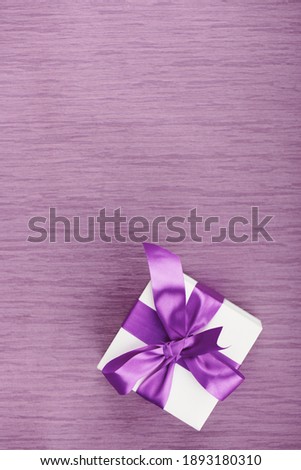 One gift box with purple bow on pink background. Vertical with copy space