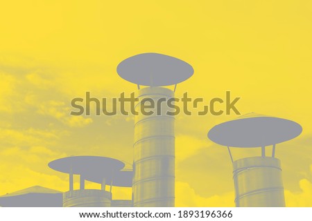 Iron chimney pipes with conical protective caps against the sky in trending colors of 2021. Abstract background of stainless steel ventilation pipes in illuminating yellow and ultimate gray color. 