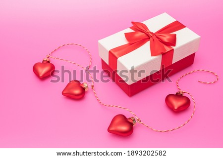 Festive gift box with bow decorated with hearts on a rope on a pink background. Copy space for text. Valentines day concept.