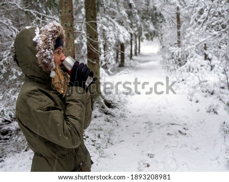 Tea keeps girl warm outside. Young woman enjoying hot drink in winter. Spruce Tree Forest 