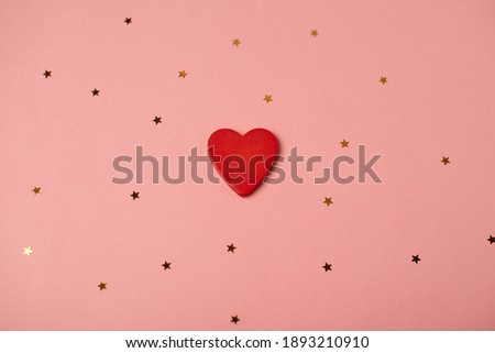 Red wooden heart and little golden stars on the rose background. Valentine's Day concept. Flat lay, top view.