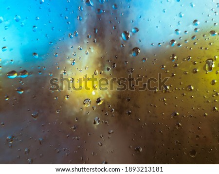 Rain drops on a window with an abstract yellow and blue background
