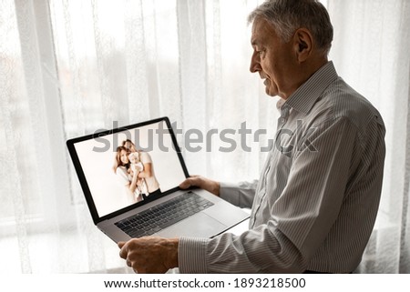 Happy caucasian grandfather hold a laptop, talking with family by internet. Mature handsome male having a video call with grandchildren. Older man use zoom, technology concept. High quality photo