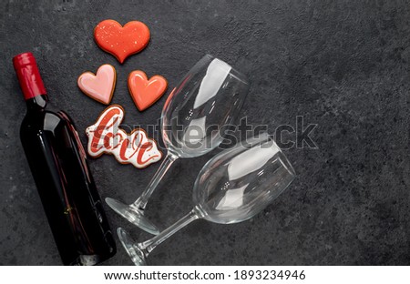 Different heart shaped cookies and one cookie with the inscription love, a bottle of wine and glasses for valentine's day
 on a stone background with copy space for your text