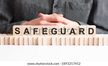 The hand puts a wooden cube with the letter SAFEGUARD. The word is written on wooden cubes standing on the white surface of the table.