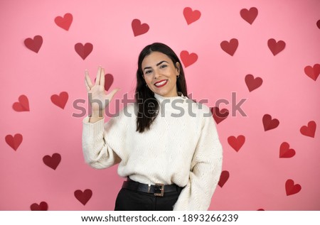 Young beautiful woman over pink background with harts doing hand symbol
