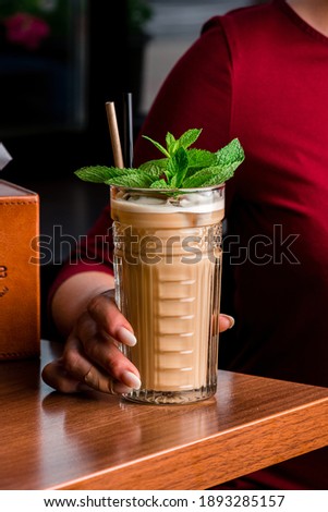 woman drinks ice cocktail with baileys in highball glass, cold coffee cocktail with milk and mint. Cold summer coffee, latte, frappe milk or non-dairy milk and mint leaves