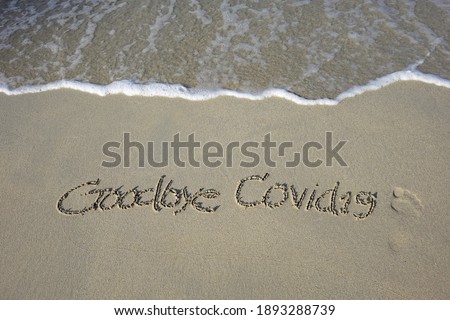 Beach sand messages : Goodbye Covid-19 written in the sand on beach with footprints and wave. Concepts photography. Selective focus 