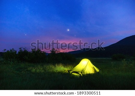 Illuminated yellow green camping tent at twilight with stars