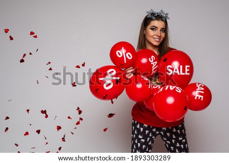 Smiling young girl with red balloons, heart shaped confetti on gray background with copy space for ad, sale concept