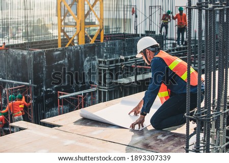 Engineer in hardhat and orange jacket posing on building site. civil engineer or architect with hardhat on construction site checking schedule on plan.