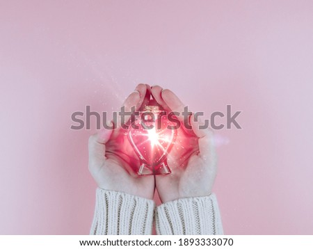 A woman holds in her palms a bottle in the shape of a heart with a red drink in the middle on a pink background, top view close-up.