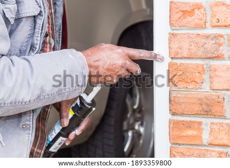 Elderly African American carpenter uses finger to apply quick dry caulk to garage facing. Royalty-Free Stock Photo #1893359800