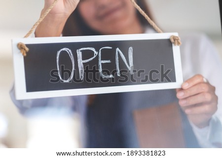 A young asian entrepreneur or a waitress hanging open sign on the shop front door 