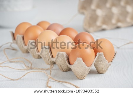 Raw brown dozen fresh chicken eggs in opened box made of recycled paper on white wooden background at kitchen. Healthy eating and sustainable consumption concept. Horizontal orientation image