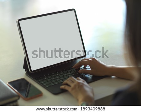 Close up view of female hands typing on tablet keyboard with smartphone and notebook on the table