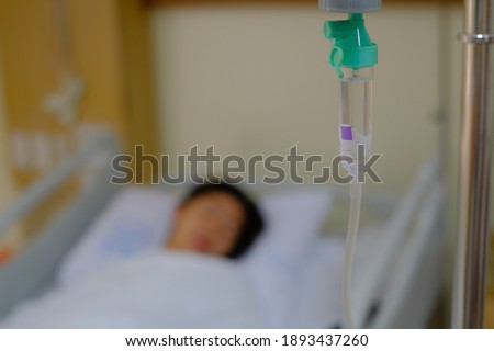 An out of focus picture of a woman resting in her hospital bed after a surgery, sleeping with an iv line dripping saline and medicine to her vein. 