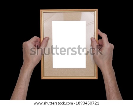 A man hangs a wooden photo frame on the walll. Isolated on black