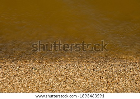 View of the calm sea water washing the sandy beach. Shredded seashells in the surf. Minimalistic natural background for relaxation. Copy space.