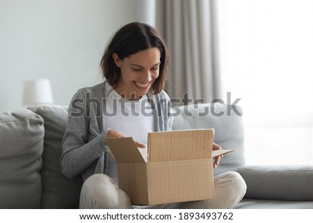 Close up overjoyed smiling young woman opening cardboard box with awaited parcel, sitting on couch at home, satisfied client received online store order, good quick delivery service concept Royalty-Free Stock Photo #1893493762