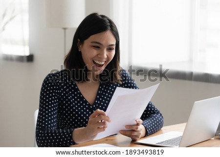 Happy millennial korean asian woman reading paper university admission notification, feeling excited alone at home. Euphoric smiling young mixed race female worker getting job promotion letter. Royalty-Free Stock Photo #1893493819