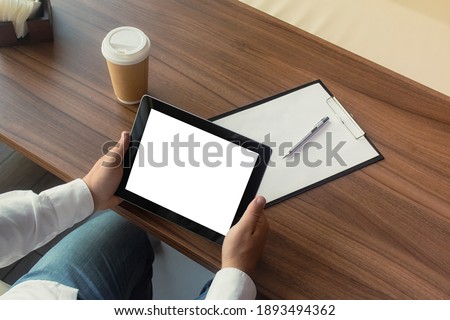 Businessman in a white shirt with a Mockup digital tablet in his hands signs a contract in the office. Workplace with a cup of coffee and a document with a pen on a wooden table.