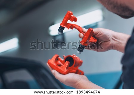 A male mechanic assembles a car brake caliper. A man holds auto parts in his hands in a car service