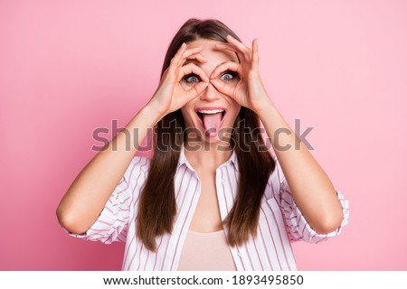 Portrait of young funky beautiful playful girl woman stick tongue out see hands binoculars isolated on pink color background