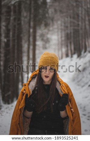 young girl scolds her partner while taking pictures in the winter. A woman aged 20-24 in a yellow jacket and black gloves stands on a snowy road. Portrait in antique white tones.