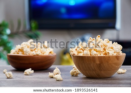 Two wooden bowls with fresh popcorn, on the background of a home interior with a TV. Royalty-Free Stock Photo #1893526141
