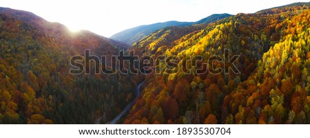 Aerial drone panorama of sun setting above the forested hills of Lotru Mountains. Autumn season, the trees are all colored. Dusk time - only the peaks of the crests are illuminated by the sun rays. Royalty-Free Stock Photo #1893530704
