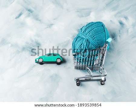 Blue wool knitting yarn in shopping cart and toy car, flat lay. Yarn delivery concept
