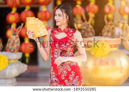 Portrait Asian young woman wearing red traditional Chinese cheongsam decoration holding yellow envelopes with the Chinese text Blessings written on it Is a Good luck for Chinese New Year Festival