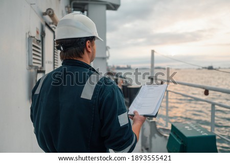 Marine Deck Officer or Chief mate on deck of offshore vessel or ship doing check and filling checklist. Paperwork at sea. Ship is on background Royalty-Free Stock Photo #1893555421