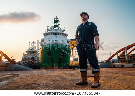 Marine Deck Officer or Chief mate on deck of offshore vessel or ship , wearing PPE personal protective equipment - helmet, coverall. Ship is on background Royalty-Free Stock Photo #1893555847