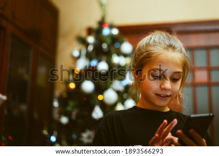 Funny little girl playing on her smartphone on Christmas Eve