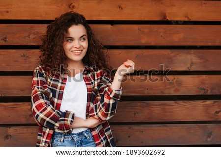 Fashion pretty young woman with curly hair wearing red checkered shirt and jeans over wooden background