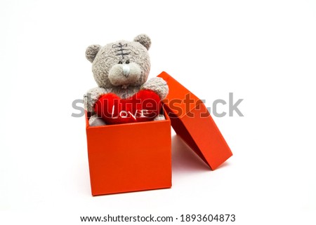 Teddy bear in a gift box with a heart in his paws, white background. 