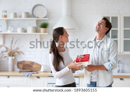 Young happy couple at home, man offering a gift to his girlfriend and making her very happy. To give gifts.